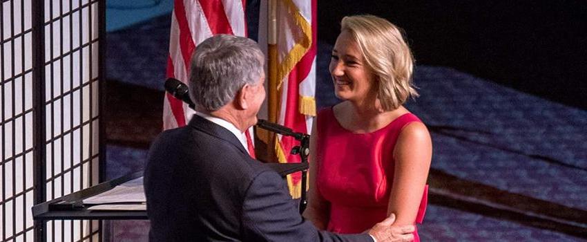 Female student walking across stage shaking dean's hand at graduation.