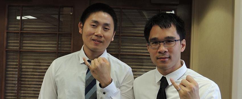 Two male students holding up their pinky rings.