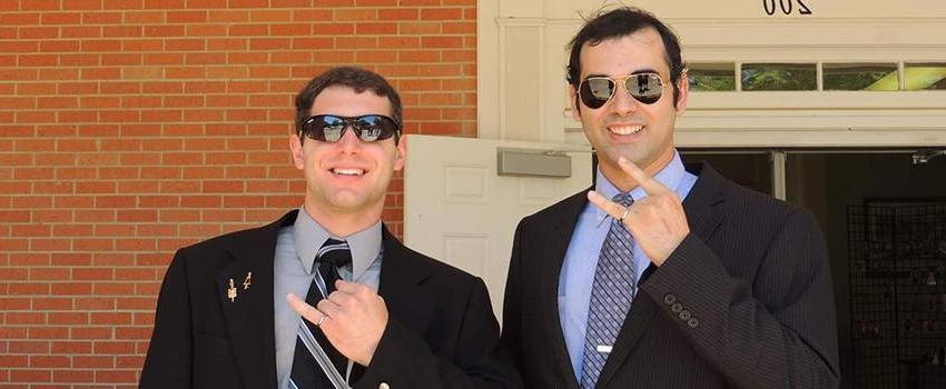 Two male students holding up their pinky rings.